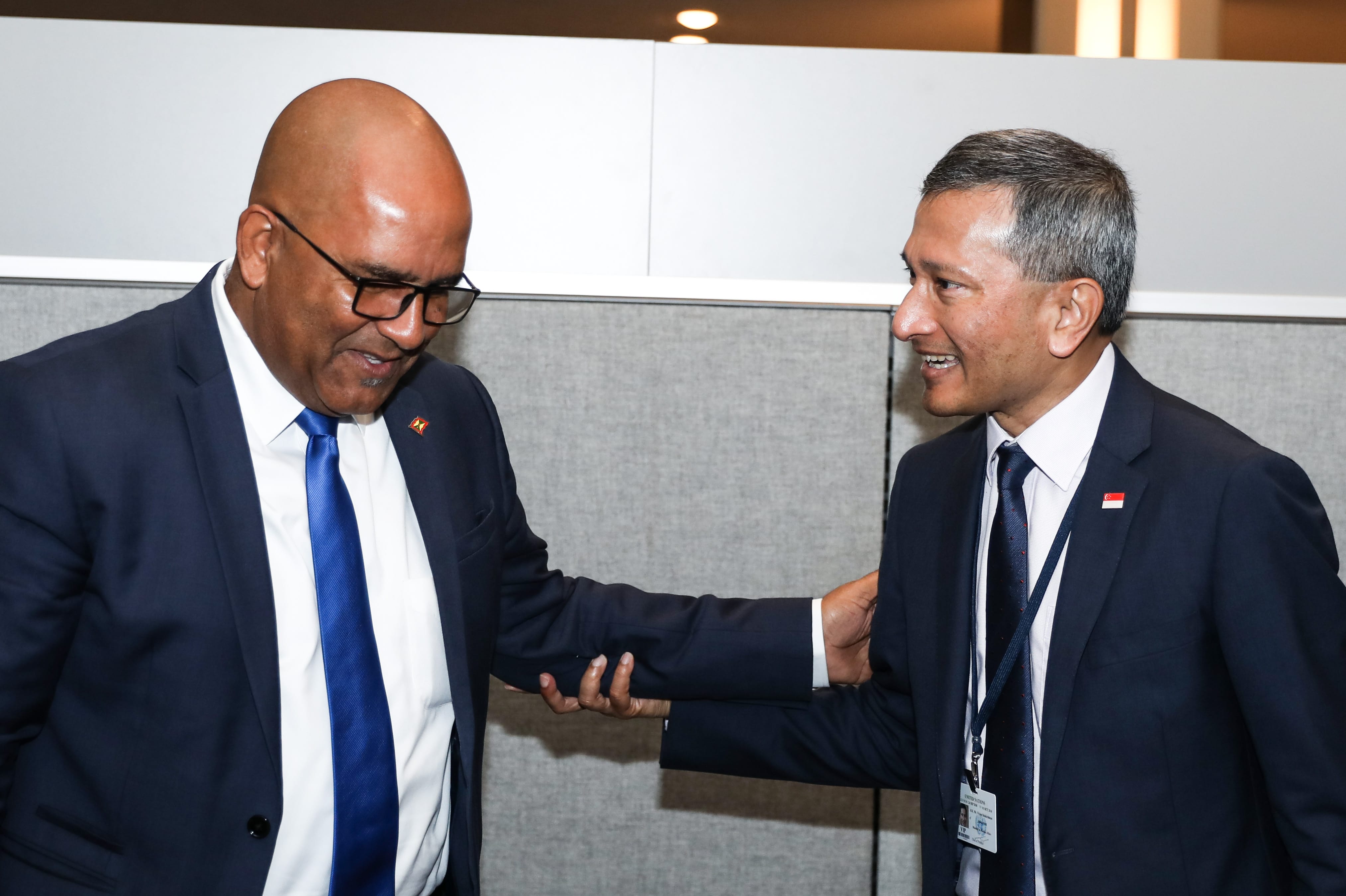 Two men in suits clasping forearms; each has lapel pin of a different flag.